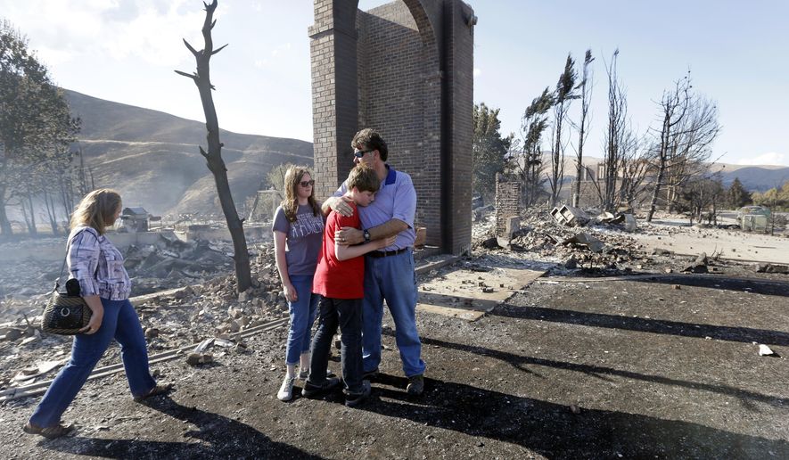 Vern Smith, right, embraces his son Spencer, 13, as daughter Mary, 17, stands with them and his wife, Julie, joins them in front of the remains of their fire-destroyed home Monday, June 29, 2015, in Wenatchee, Wash. The wildfire fueled by high temperatures and strong winds roared into town Sunday afternoon. The blaze ignited in brush just outside Wenatchee, quickly burning out of control. (AP Photo/Elaine Thompson)