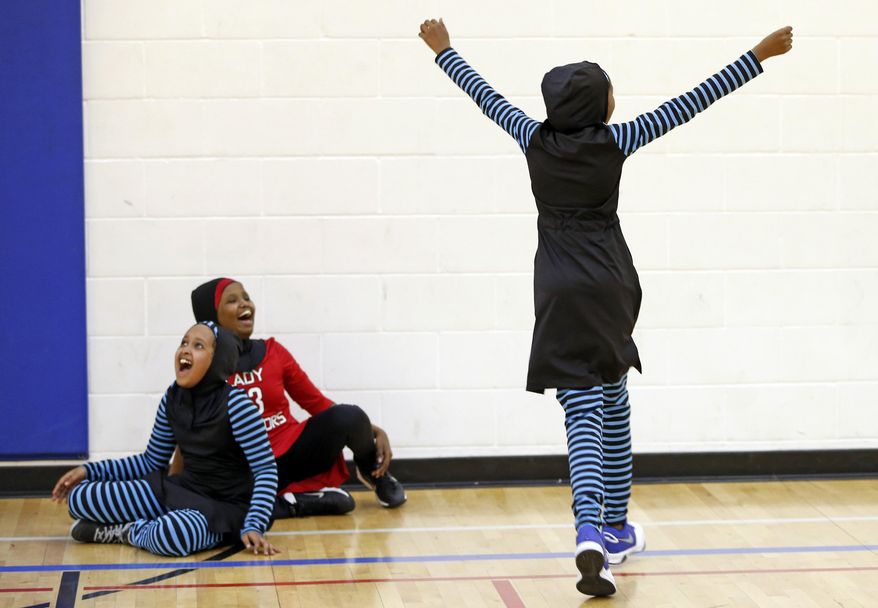 In this June 16, 2015, file photo, Ramla Ali, left, and Amira Ali, on Ramia's right, help celebrate a basket at an East African Muslim girls basketball practice in Minneapolis. Muslim girls who play sports have challenges that go beyond the sporting. Their new culturally sensitive uniforms, designed by the girls, address worries over tripping on a long, flowing dress, or having a loosely wrapped hijab come undone during a crucial play. (AP Photo/Jim Mone) ** FILE **