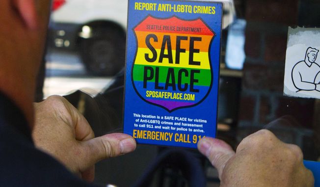 In this June 24, 2015, photo, Officer Jim Ritter places a “Safe Place” sticker on the window of a business in Seattle&#x27;s Capitol Hill neighborhood. Last September, after more than three decades on the force, Ritter, 54, was appointed as SPD&#x27;s first full-time liaison to the city&#x27;s LGBTQ community. (Ellen M. Banner(/The Seattle Times via AP)
