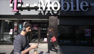 A man uses a cellphone as he passes a T-Mobile store in New York. (AP Photo/Mark Lennihan, File)