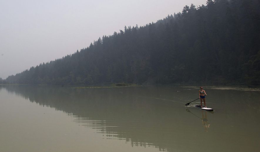 Smoke from wildfires fills the air as Lisa Fogarty paddleboards at One Mile Lake in Pemberton, in Pemberton, British Columbia, Wednesday, July 8, 2015. Firefighters made some progress Wednesday in quelling hundreds of wildfires raging across central and western Canada that are threatening thousands of people and triggering air quality warnings across the country and in the U.S. West and Midwest, authorities said. (Darryl Dyck/The Canadian Press via AP) MANDATORY CREDIT