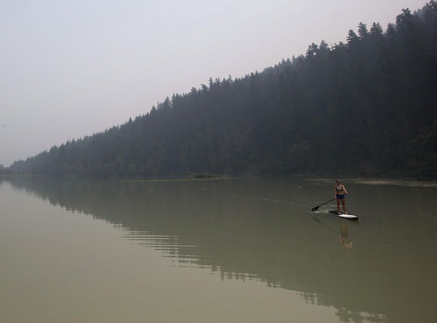 Smoke from wildfires fills the air as Lisa Fogarty paddleboards at One Mile Lake in Pemberton, in Pemberton, British Columbia, Wednesday, July 8, 2015. Firefighters made some progress Wednesday in quelling hundreds of wildfires raging across central and western Canada that are threatening thousands of people and triggering air quality warnings across the country and in the U.S. West and Midwest, authorities said. (Darryl Dyck/The Canadian Press via AP) MANDATORY CREDIT