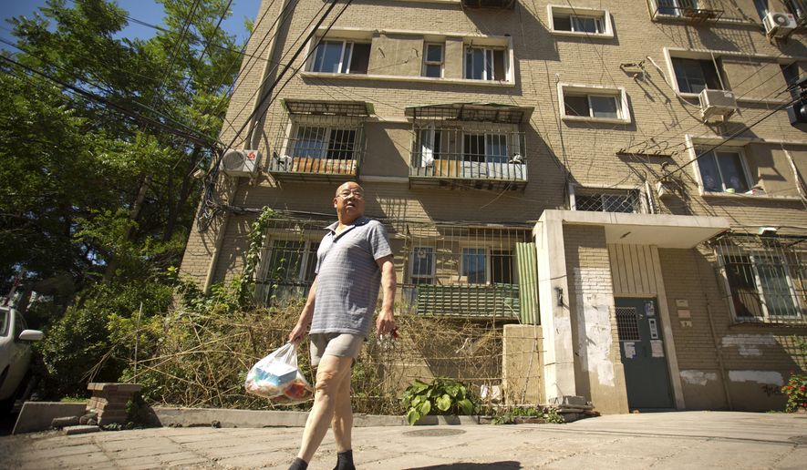 In this Thursday, June 18, 2015 photo, a man walks outside a building in Beijing where an apartment is listed in Chinese official documents as being registered to Xu Ting, her younger brother Xu Lei, and their mother Zhao Peiyuan. Xu Ting, a Chinese immigrant living in the U.S has been sued for counterfeiting by eight different luxury brands, including Gucci and Louis Vuitton, and still owes Chanel Inc. $6.9 million in damages for counterfeiting, according to U.S. court documents. None of this has stopped her from becoming a lawful permanent resident of the United States and amassing the trappings of a solid middle class life. (AP Photo/Mark Schiefelbein)