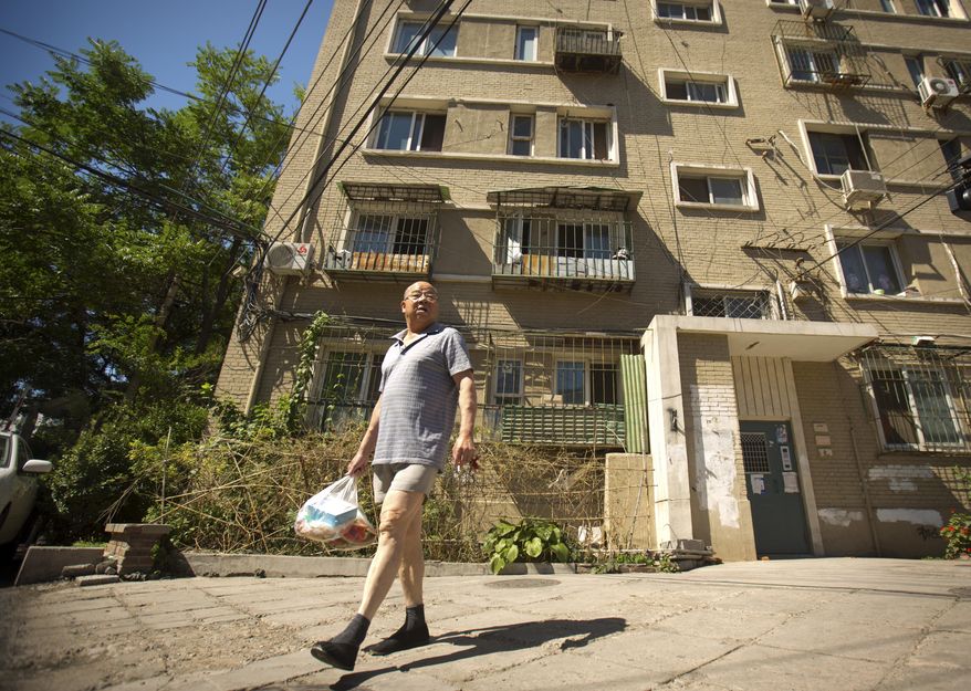 In this Thursday, June 18, 2015 photo, a man walks outside a building in Beijing where an apartment is listed in Chinese official documents as being registered to Xu Ting, her younger brother Xu Lei, and their mother Zhao Peiyuan. Xu Ting, a Chinese immigrant living in the U.S has been sued for counterfeiting by eight different luxury brands, including Gucci and Louis Vuitton, and still owes Chanel Inc. $6.9 million in damages for counterfeiting, according to U.S. court documents. None of this has stopped her from becoming a lawful permanent resident of the United States and amassing the trappings of a solid middle class life. (AP Photo/Mark Schiefelbein)