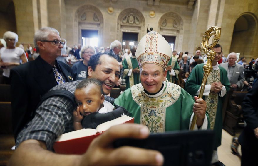 Aime held his son Raphael take a selfie with Archbishop Bernard Hebda after his first Mass at the St. Paul Cathedral, Sunday, July 12, 2015, in St. Paul Minn. (Jerry Holt/Star Tribune via AP) MANDATORY CREDIT; ST. PAUL PIONEER PRESS OUT; MAGS OUT; TWIN CITIES LOCAL TELEVISION OUT