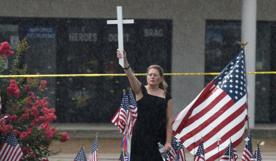 Lisa Camp holds a cross in the rain near the Armed Forces Career Center on Lee Highway, Sunday, July 19, 2015, in Chattanooga, Tenn. Muhammad Youssef Abdulazeez attacked two military facilities, including the career center, last week in a shooting rampage that killed a U.S. Navy sailor and four Marines. (John Rawlston/Chattanooga Times Free Press via AP)