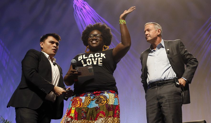 As dozens protesters shout, Tia Oso of the National Coordinator for Black Immigration Network, center, walks up on stage interrupting Democratic presidential candidate, former Maryland Gov. Martin O&#x27;Malley, right, as moderator Jose Vargas watches at left, during the Netroots Nation town hall meeting, Saturday, July 18, 2015, in Phoenix. (AP Photo/Ross D. Franklin)