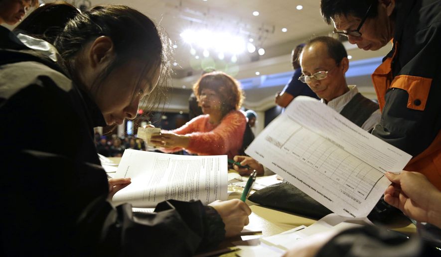 Christina Hung (left), 23, of Oakland, fills out an application form during a health care enrollment event at the Oakland Asian Cultural Center in Oakland, Calif., on March 31, 2014. State-run health insurance markets that offer taxpayer-subsidized coverage under President Barack Obama’s law are grappling with high costs and disappointing enrollment, challenges that could lead more of them to turn over functions to the federal government, or join forces with other states. (Associated Press) **FILE**