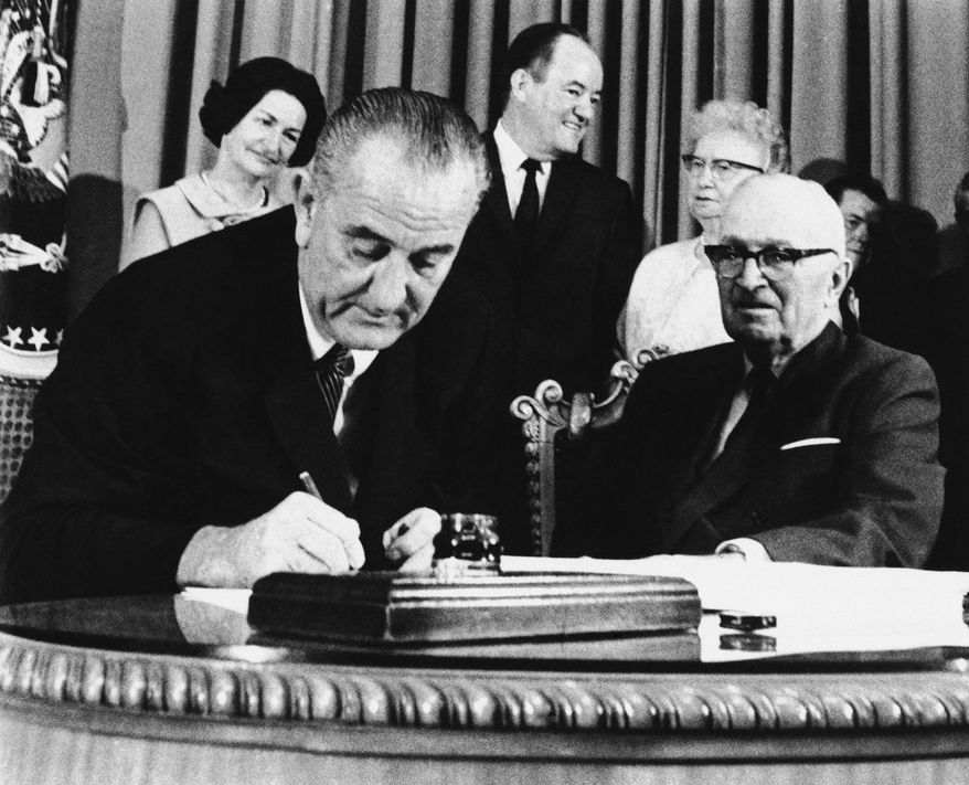 FILE - In this July 30, 1965 file photo, President Lyndon Johnson signs the Medicare Bill into law while former President Harry S. Truman, right, observes during a ceremony at the Truman Library in Independence, Mo. At rear are Lady Bird Johnson, Vice President Hubert Humphrey, and former first lady Bess Truman. When Johnson signed Medicare and Medicaid into law Americans 65 and older were the age group least likely to have health insurance.  (AP Photo)