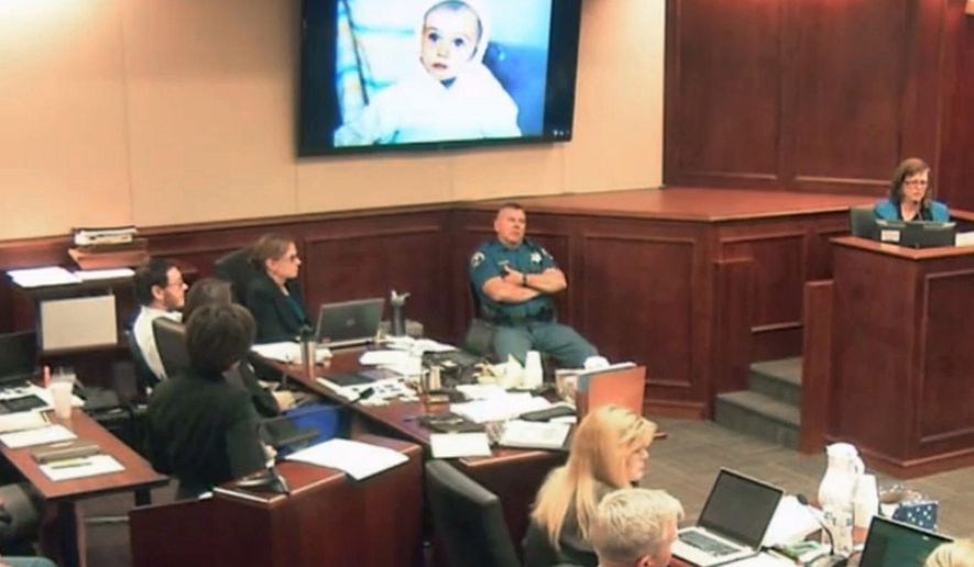 FILE - In this July 29, 2015 file image made from Colorado Judicial Department video, a family photo is displayed on the screen showing James Holmes when he was a toddler, as James Holmes' mother Arlene, top right, gives testimony during the sentencing phase of the Colorado theater shooting trial in Centennial, Colo. James Holmes sits in court at far left. A fuller portrait of the Colorado movie theater shooter has emerged during Holmes' death penalty trial. Testimony given by Holmes' parents revealed a family laid bare by the tragic consequences of a son's incomprehensible descent from a well–behaved child with a quirky sense of humor into a killer capable of gunning down defenseless strangers. (Colorado Judicial Department via AP, Pool, File)