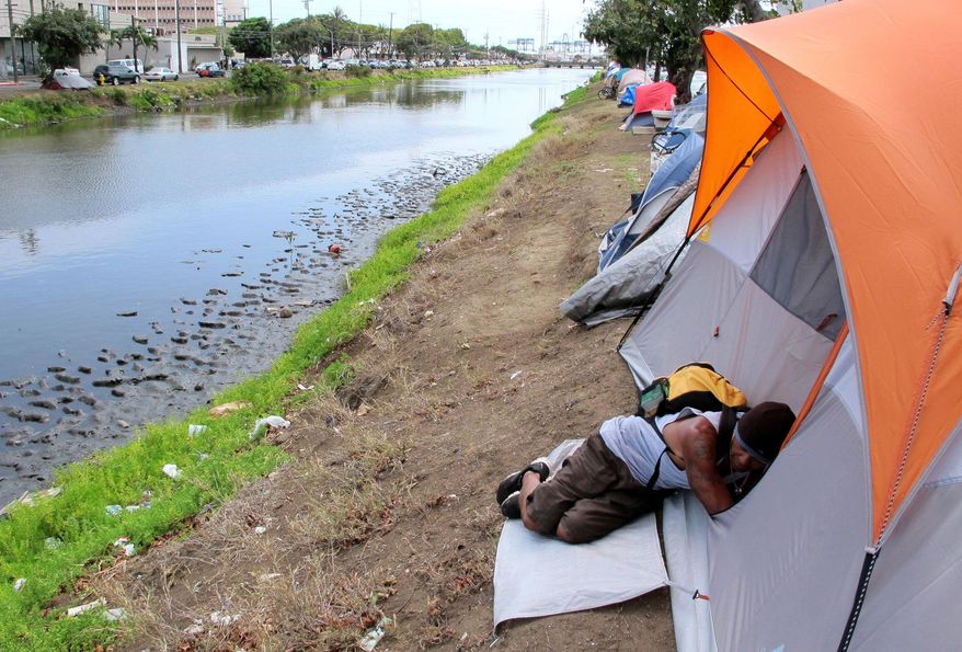 FILE - In this April 22, 2015 file photo, photo, Derek Villanueva, who is homeless, sleeps outside a friend’s tent in an encampment along a canal in Honolulu. The Honolulu City Council was voting Wednesday, Aug. 5, 2015, to expand a ban on sitting and lying down in parts of Honolulu to the banks of city-owned streams and pedestrian malls in downtown and Chinatown. (AP Photo/Cathy Bussewitz, File)