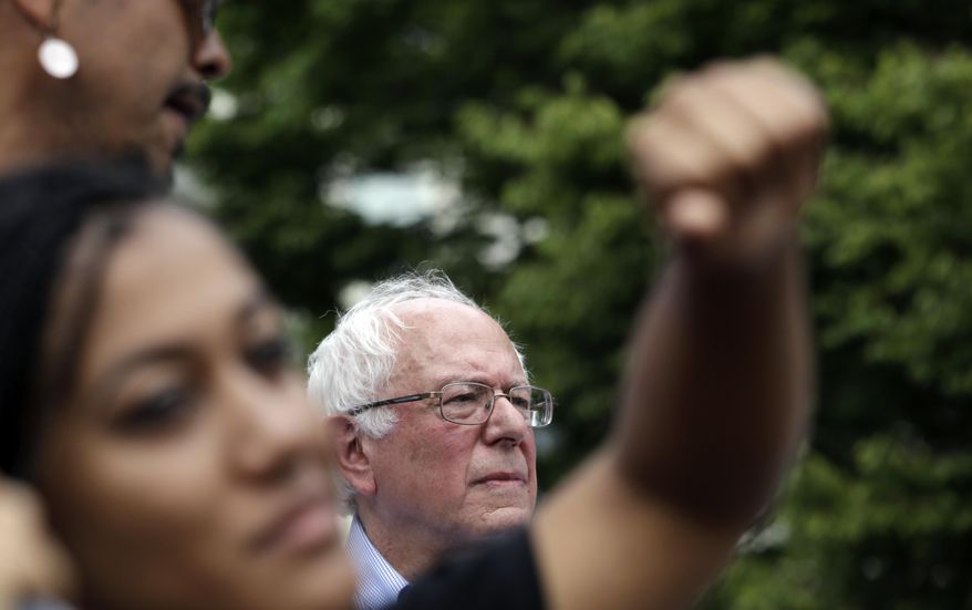 Mara Jacqueline Willaford, left, holds her fist overhead as Democratic presidential candidate Sen. Bernie Sanders, I-Vt., stands nearby at a rally Saturday, Aug. 8, 2015, in downtown Seattle. Willaford and another co-founder of the Seattle chapter of Black Lives Matter took over the microphone just after Sanders began to speak and refused to relinquish it. Sanders eventually left the stage without speaking further and instead waded into the crowd to greet supporters. (AP Photo/Elaine Thompson)