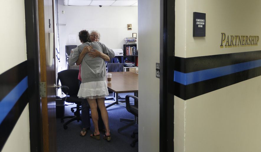 In this July 10, 2015, photo, volunteer Ruth Cote, facing, hugs a woman inside the police station in Gloucester, Mass., who has voluntarily come to the police for help kicking her heroin addiction. Gloucester is taking a novel approach to the war on drugs, making the police station a first stop for addicts on the road to recovery. Addicts can turn in their drugs to police, no questions asked, and officers, volunteers and trained clinicians help connect them with detox and treatment services. (AP Photo/Elise Amendola)