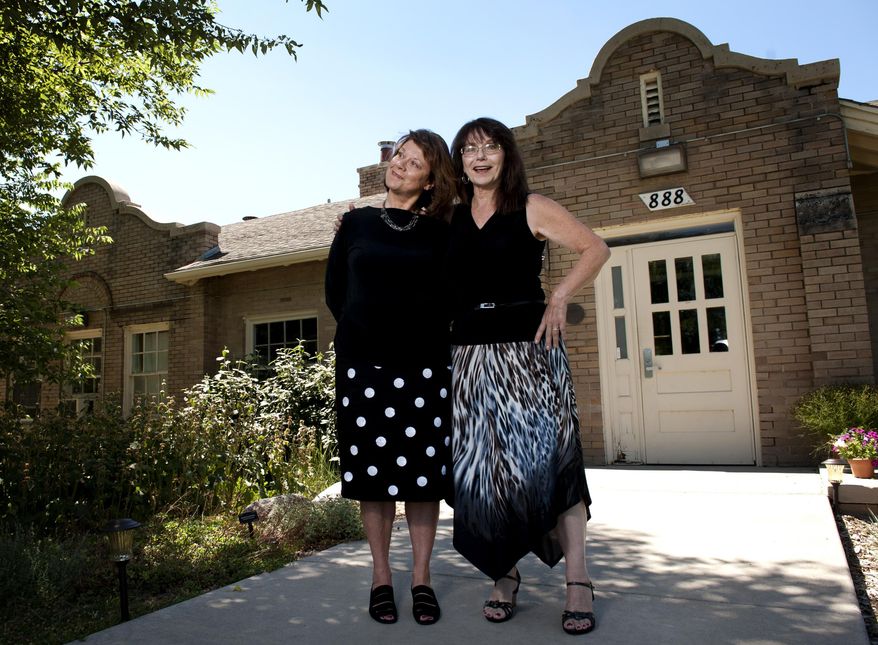 In this July 28, 2015 photo, Shayne Madsen, left, stands with her long-lost sister, Diane Lippoldt-Johnson, right, in front of what was once an orphanage in Denver. (Ryan Gooding/Daily Camera via AP) NO SALES; MANDATORY CREDIT