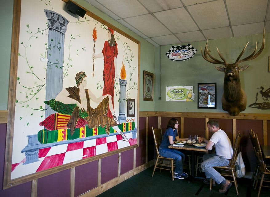 In this photo taken Sunday, Aug. 9, 2015, Glynis Frederiksen and Brian Campbell of Seattle have lunch in the light of a mural painted by local boy makes good, Chris Pratt, at Omega Pizza and Pasta in Granite Falls, Wash. Pratt, best friends with the owner's son, has been known to tie on an apron and help out in the kitchen on one his recent visits. (Kevin Clark/The Herald via AP) MANDATORY CREDIT