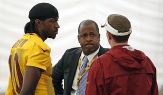 Washington Redskins quarterback Robert Griffin III, left, talks with Tony Wyllie, center, Redskins senior vice president for communications, and Ross Taylor, director of communications, after NFL football practice, Tuesday, Aug. 18, 2015, in Ashburn, Va. Griffin later spoke with reporters. (AP Photo/Alex Brandon) **FILE**