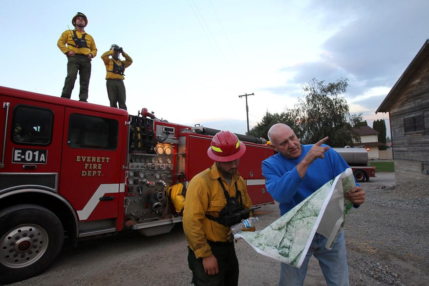 In this photo taken on Friday, Aug. 21, 2015, Omak resident Pat Charles, right, shows Lake Roesiger firefighter Scott Anderson a map of the back roads in the hills above his house as Everett Fire crew members Matt Park, left, and Captain Brent Stainer keep a look out on an encroaching fire, as wildfires continue to burn throughout north-central Washington. (Genna Martin/The Herald via AP) MANDATORY CREDIT
