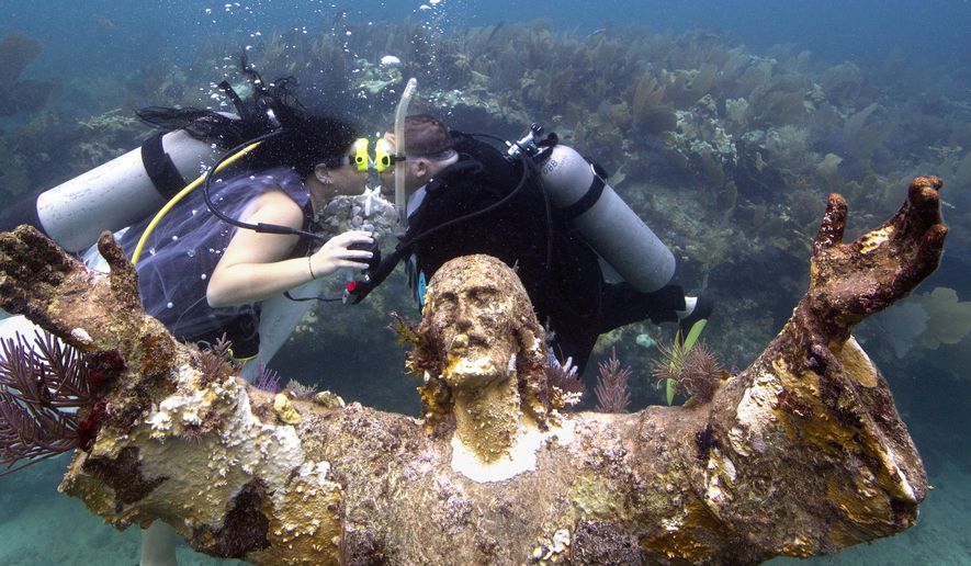 In this photo provided by the Florida Keys News Bureau, Kimberly Triolet, left, and Jorge Rodriguez, right, kiss after being married next to the Christ of the Deep statue Tuesday, Aug. 25, 2015, in the Florida Keys National Marine Sanctuary off Key Largo, Fla. The wedding helped to mark the 50th anniversary of the installation of the 9-foot-tall bronze sculpture that is a symbol for Key Largo's John Pennekamp Coral Reef State Park, America's first underwater preserve that is part of the sanctuary. It is a replica of the "Christ of the Abyss" that was placed in Italian waters in 1954. (Bob Care/Florida Keys News Bureau via AP)