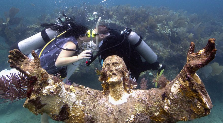 In this photo provided by the Florida Keys News Bureau, Kimberly Triolet, left, and Jorge Rodriguez, right, kiss after being married next to the Christ of the Deep statue Tuesday, Aug. 25, 2015, in the Florida Keys National Marine Sanctuary off Key Largo, Fla. The wedding helped to mark the 50th anniversary of the installation of the 9-foot-tall bronze sculpture that is a symbol for Key Largo's John Pennekamp Coral Reef State Park, America's first underwater preserve that is part of the sanctuary. It is a replica of the "Christ of the Abyss" that was placed in Italian waters in 1954. (Bob Care/Florida Keys News Bureau via AP)
