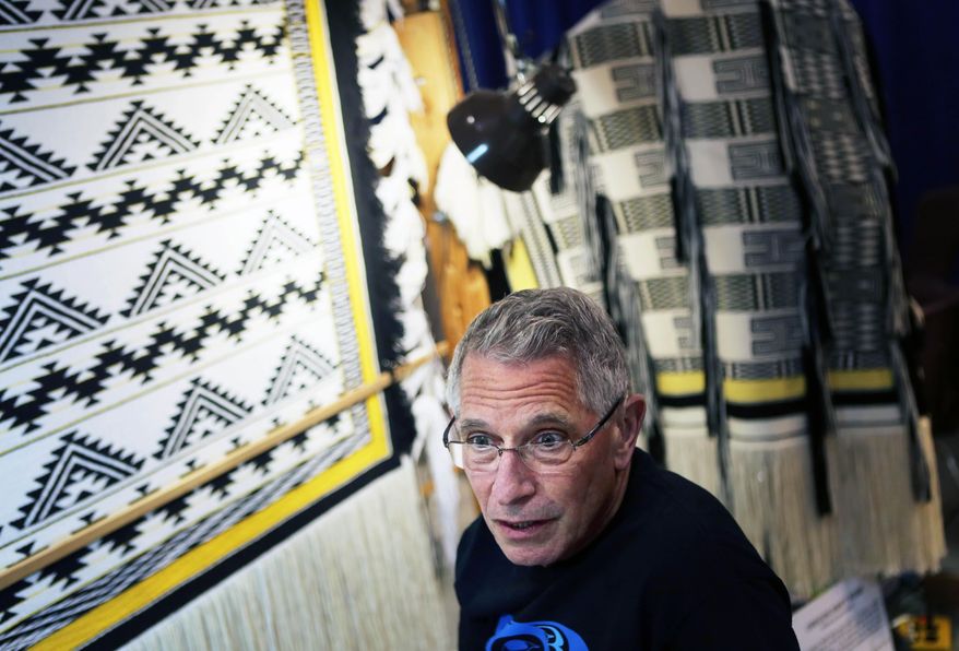 In this Aug. 2014 photo, Salem native John Beard stands before his Ravenstail weaving display at the 2014 Oregon State Fair in Salem, Ore.. Salem native John Beard of Tigard has been making connections at the Oregon State Fair for more than three decades. He’s made connections between warp and weft, the vertical and horizontal yarns that he weaves on his loom, but demonstrating the art of Ravenstail weaving is about more than the large and beautiful ceremonial robes he produces. (Thomas Patterson/Statesman-Journal via AP) MANDATORY CREDIT