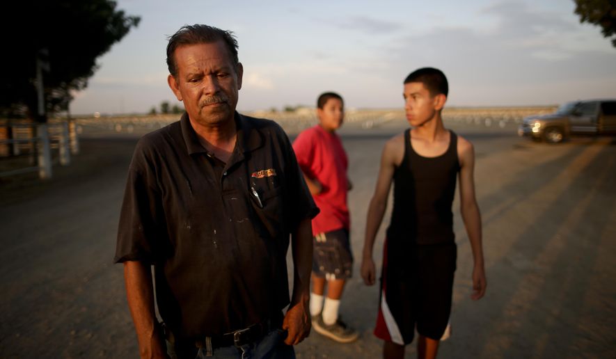 In this June 30, 2015 photo, Gilbert Arredondo, left, looks down as he talks about his town's water crisis, standing in front of his tenant's sons, in the community of Okieville, on the outskirts of Tulare, Calif. Arredondo had just informed his tenant, Tino Lozano, that the well connecting their houses had gone dry. The water is disappearing at a particularly alarming pace in their neighborhood, forcing neighbors to rig lines from house to house to share what underground water is still reachable from the deepest wells. (AP Photo/Gregory Bull)