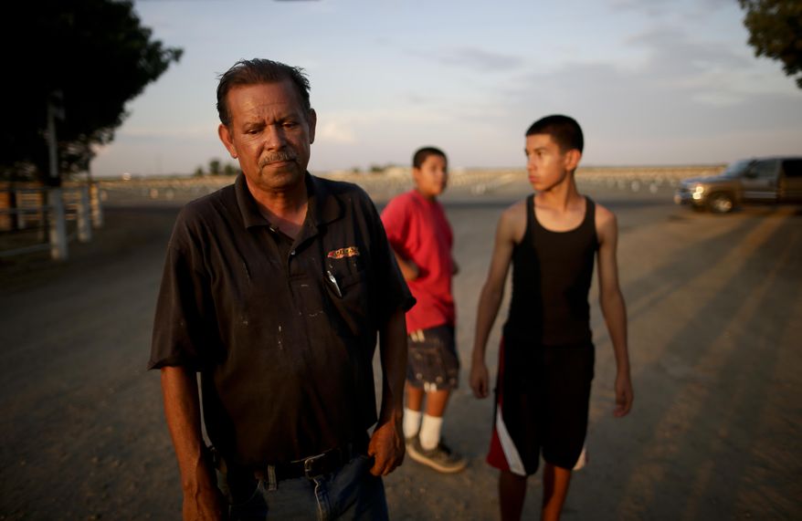 In this June 30, 2015 photo, Gilbert Arredondo, left, looks down as he talks about his town's water crisis, standing in front of his tenant's sons, in the community of Okieville, on the outskirts of Tulare, Calif. Arredondo had just informed his tenant, Tino Lozano, that the well connecting their houses had gone dry. The water is disappearing at a particularly alarming pace in their neighborhood, forcing neighbors to rig lines from house to house to share what underground water is still reachable from the deepest wells. (AP Photo/Gregory Bull)