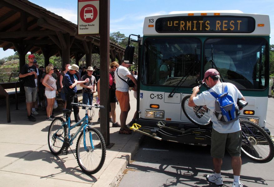 In this Wednesday, Aug. 19, 2015 photo, David Stonecypher, right, of Duarte, Calif., loads his bike on a shuttle bus at Grand Canyon National Park in northern Arizona. Grand Canyon and other big national parks are seeing more visitors than usual this year, partly driven by good weather, cheap gas and marketing campaigns. (AP Photo/Felicia Fonseca)