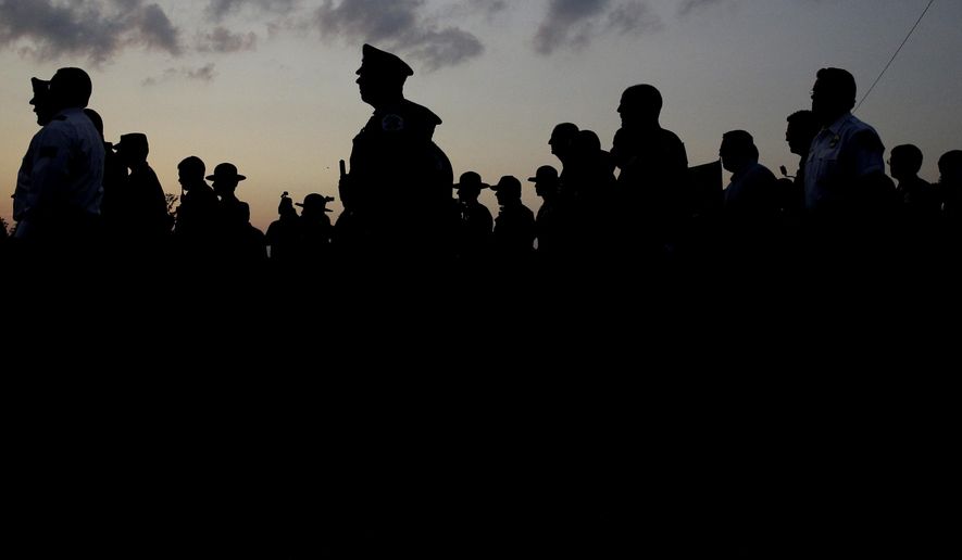 Police officials follow Fox Lake Police Lt. Charles Joseph Gliniewicz's family after a vigil at Lakefront Park to honor him on Wednesday, Sept. 2, 2015, in Fox Lake, Ill. Gliniewicz was shot and killed Tuesday while pursuing a group of suspicious men. Police are searching for a second day to locate three suspects in the killing. (AP Photo/Nam Y. Huh)