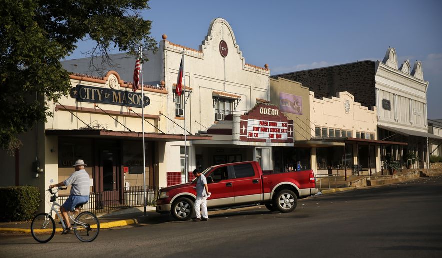 A cyclist rides pass the Mason City Hall and the Odeon Theatre on Aug. 14, 2015. A proposal by an Italian energy developer to build a wind farm in the heart of Hill Country has stirred up intense opposition among locals, who say the 400-foot turbines will ruin the picturesque town that draws thousands of tourists every year. Of particular concern is the local population of Mexican free-tailed bats, which studies show have been killed off when they fly to close to the spinning blades. (Tom Fox/The Dallas Morning News via AP) MANDATORY CREDIT; MAGS OUT; TV OUT; INTERNET USE BY AP MEMBERS ONLY; NO SALES