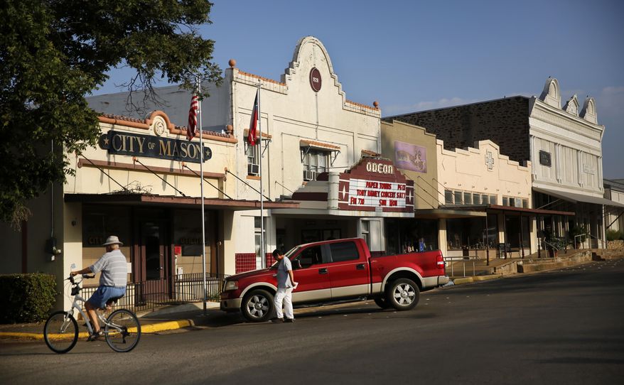 A cyclist rides pass the Mason City Hall and the Odeon Theatre on Aug. 14, 2015. A proposal by an Italian energy developer to build a wind farm in the heart of Hill Country has stirred up intense opposition among locals, who say the 400-foot turbines will ruin the picturesque town that draws thousands of tourists every year. Of particular concern is the local population of Mexican free-tailed bats, which studies show have been killed off when they fly to close to the spinning blades. (Tom Fox/The Dallas Morning News via AP) MANDATORY CREDIT; MAGS OUT; TV OUT; INTERNET USE BY AP MEMBERS ONLY; NO SALES