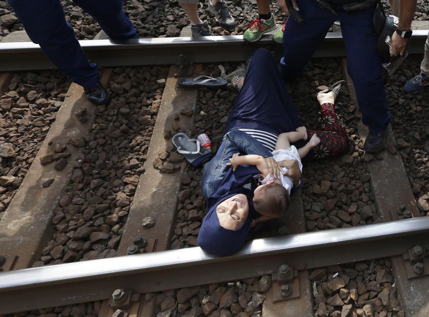 A migrant lies on the track with a baby as she is detained in Bicske, Hungary, Thursday, Sept. 3, 2015. Over 150,000 migrants have reached Hungary this year, most coming through the southern border with Serbia. Many apply for asylum but quickly try to leave for richer EU countries. (AP Photo/Petr David Josek)