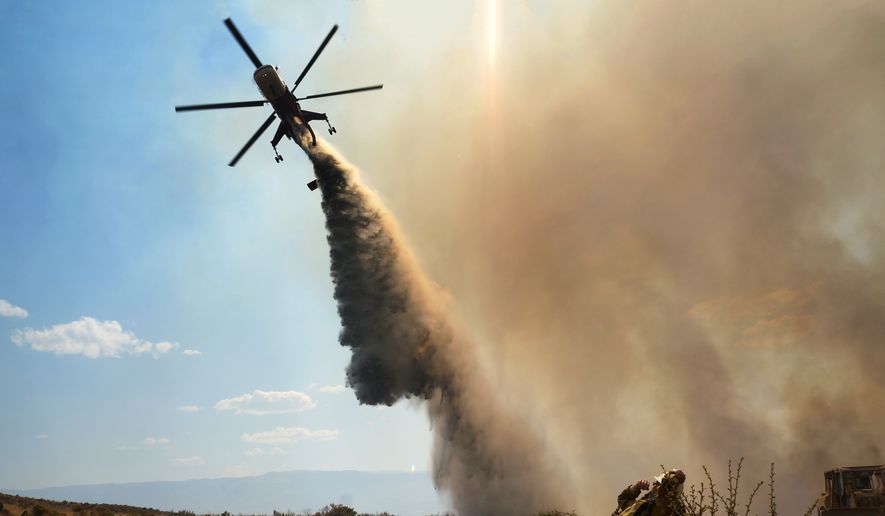 This Aug. 9, 2015, photo taken by Utah state firefighter Eli Peterson shows a firefighter watching as a helicopter makes a water drop over a fire in Owyhee County, Idaho. (Eli Peterson via AP) ** FILE **