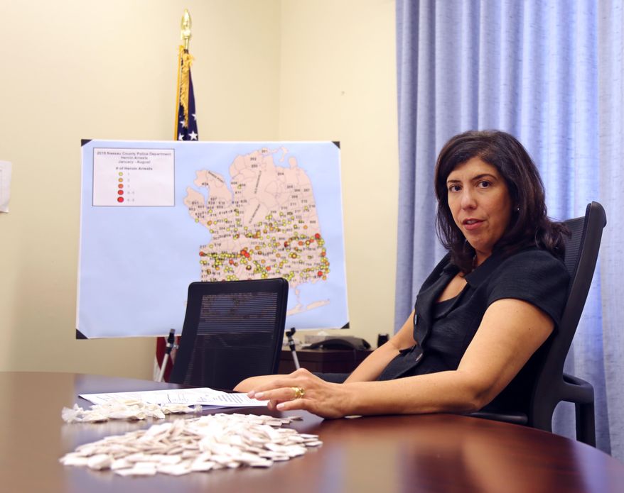Acting Nassau County District Attorney Madeline Singas motions over packets of heroin piled on her desk, Wednesday, Sept. 9, 2015, in Mineola, N.Y. Aiming to curb rising heroin use in the suburbs of New York City, prosecutors on Long Island have written legislation that would allow authorities to charge heroin dealers with homicide after fatal overdoses. (AP Photo/Mike Balsamo)