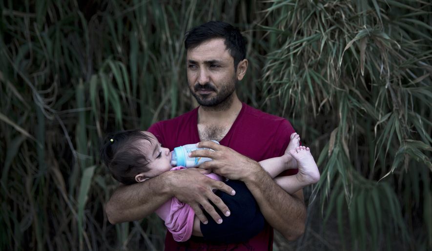 A Syrian refugee feeds milk to his daughter after they arrived on a dinghy, from Turkey to Lesbos island, Greece, Wednesday, Sept. 9, 2015. The head of the European Union's executive says 22 of the member states should be forced to accept another 120,000 people in need of international protection who have come toward the continent at high risk through Greece, Italy and Hungary. (AP Photo/Petros Giannakouris)