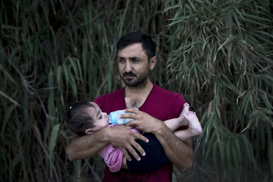 A Syrian refugee feeds milk to his daughter after they arrived on a dinghy, from Turkey to Lesbos island, Greece, Wednesday, Sept. 9, 2015. The head of the European Union's executive says 22 of the member states should be forced to accept another 120,000 people in need of international protection who have come toward the continent at high risk through Greece, Italy and Hungary. (AP Photo/Petros Giannakouris)