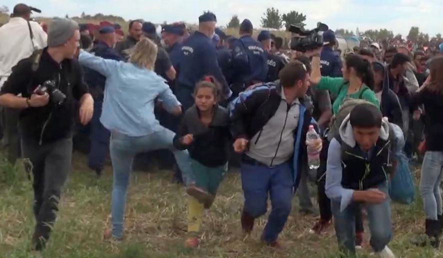 In this image taken from TV a Hungarian camerawoman, center left in blue, kicks out at a young migrant who had just crossed the border from Serbia near Roszke Hungary Tuesday, Sept. 8, 2015. The camerawoman has been fired after she was caught on video kicking and tripping migrants entering Hungary across the border with Serbia. (Index.Hu. via AP)