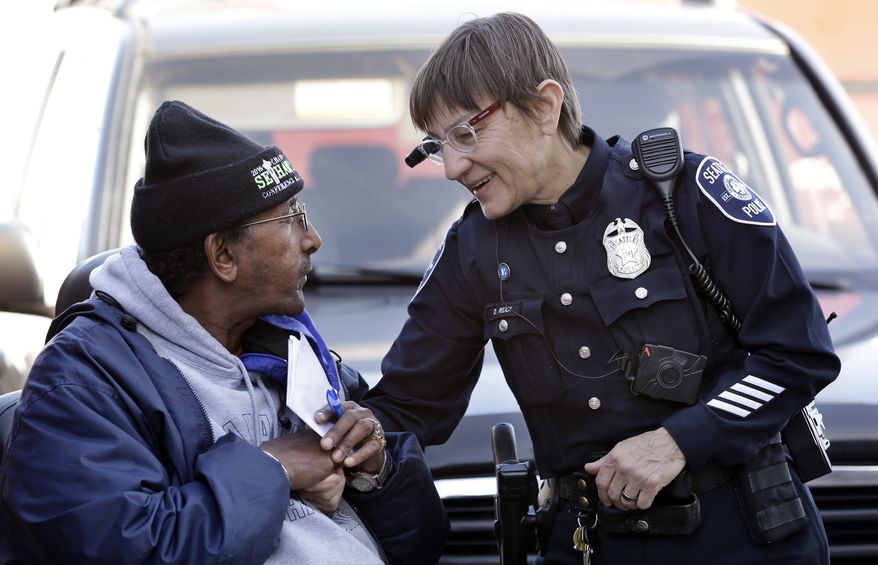 Seattle police officer Debra Pelich, right, wears a video camera on her eyeglasses as she talks with Alex Legesse before a small community gathering in Seattle, in this March 12, 2015, file photo. The camera is attached to a battery pack and controls on the officer's uniform. (AP Photo/Elaine Thompson, File)