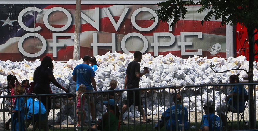 In this Aug. 15, 2015, file photo, volunteers and patrons of a Convoy of Hope event walk past bagged groceries as they exit a park in O’Fallon, Ill. Convoy of Hope, based in Springfield, Mo., is an interdenominational organization that provides assistance to those in need. (Tim Vizer/Belleville News-Democrat via AP) ** FILE **