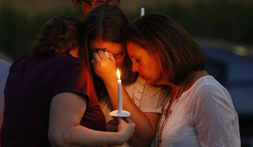 Liz Schmidt, widow of Delta State University history professor Ethan Schmidt, center, who was murdered by a colleague in his office Monday, is comforted by friends, Jenn Westmoreland, left, and Amy Cotrell, during a candlelight memorial in his honor on the Cleveland, Miss., campus, Tuesday night, Sept. 15, 2015. (AP Photo/Rogelio V. Solis)