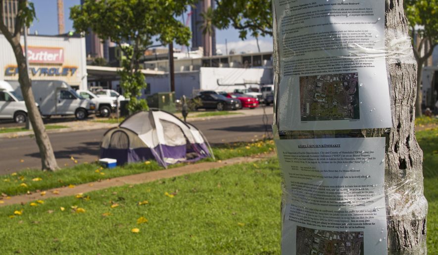 FILE - In this Sept. 8, 2015 file photo, signs posted in Chuukese and Marshallese announcing the beginning of sidewalk nuisance and stored property enforcement are posted to a palm tree in Kaka‘ako Park in Honolulu. Attorneys with the American Civil Liberties Union say the group will sue Honolulu over the way city officials are clearing out homeless encampments. The attorneys say they plan to file a lawsuit Wednesday, Sept. 16, 2015. (AP Photo/Marco Garcia)