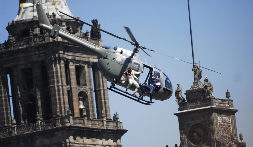 In this Monday, March 30, 2015, file photo, stunt doubles perform an action scene aboard a helicopter above the Zocalo, Mexico City's main square, during the filming of "Spectre," the latest of the James Bond 007 movies, in Mexico. (AP Photo/Sandra Stargardter, File)
