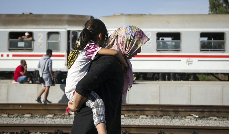 A refugee woman carries a child at a train station in Beli Manastir, near the Hungarian border, in northeast Croatia, early Friday, Sept. 18, 2015. Croatian police say some 13,300 migrants have entered the country from Serbia since the first groups started arriving more than two days ago. (AP Photo/Darko Bandic)
