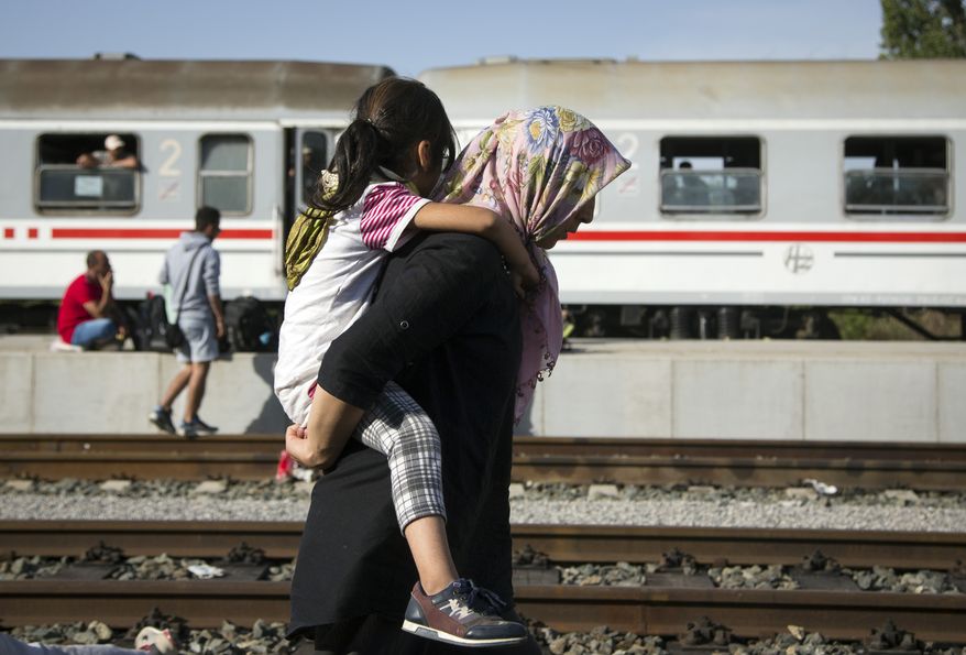 A refugee woman carries a child at a train station in Beli Manastir, near the Hungarian border, in northeast Croatia, early Friday, Sept. 18, 2015. Croatian police say some 13,300 migrants have entered the country from Serbia since the first groups started arriving more than two days ago. (AP Photo/Darko Bandic)