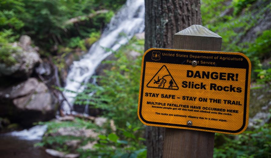 This June 7, 2015 photo, signs line the trail at Crabtree Falls, warning visitors not to stray from the path due to slippery rocks in Nelson County, Va. At least 30 people have died at Crabtree Falls in Nelson County since the U.S. Forest Service began tracking the incidents in 1982. (Autumn Parry/News & Daily Advance via AP) MANDATORY CREDIT