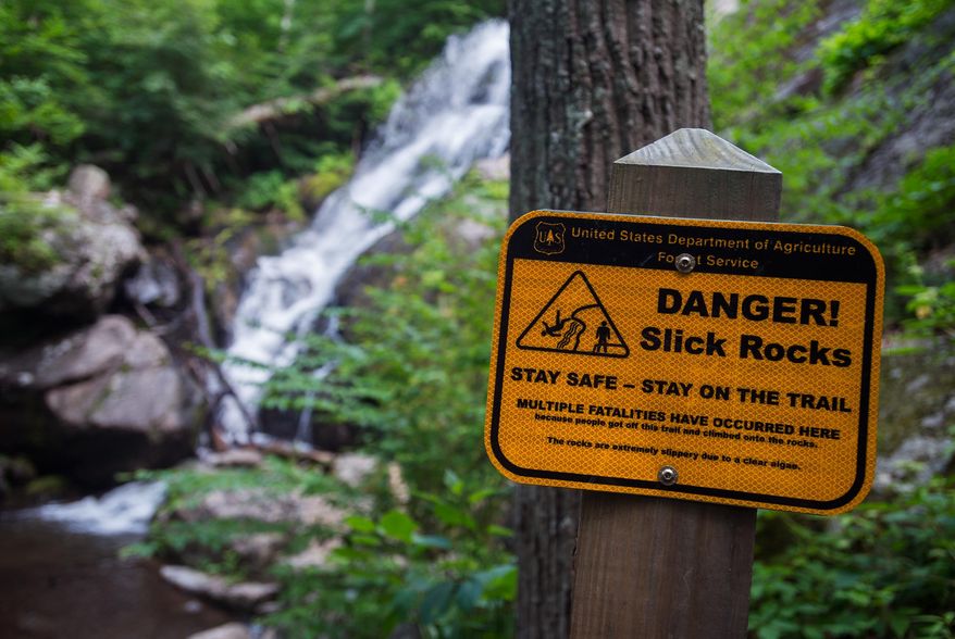 This June 7, 2015 photo, signs line the trail at Crabtree Falls, warning visitors not to stray from the path due to slippery rocks in Nelson County, Va. At least 30 people have died at Crabtree Falls in Nelson County since the U.S. Forest Service began tracking the incidents in 1982. (Autumn Parry/News & Daily Advance via AP) MANDATORY CREDIT