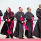 Clergy brace for the wind as they stand along the red carpet on the tarmac at Andrews Air Force Base, Md., Tuesday, Sept. 22, 2015, as the plane carrying Pope Francis arrives. (AP Photo/Andrew Harnik)