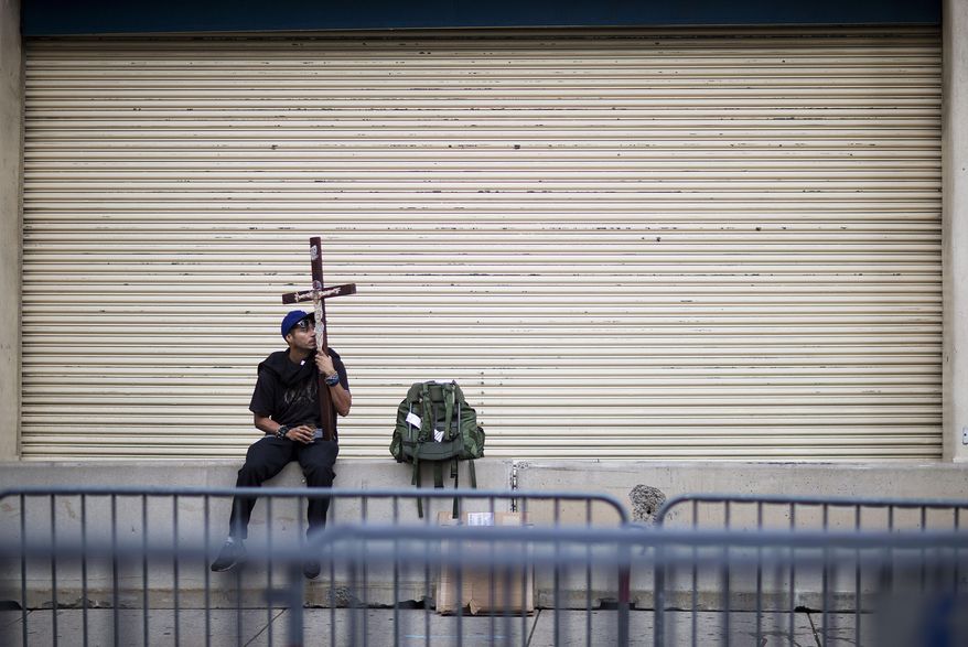 Mauro Avila, of Uvalde, Texas, sits with a cross outside a security checkpoint set up in preparation of Pope Francis' visit to Philadelphia, Friday, Sept. 25, 2015. Francis wraps up his U.S. visit this weekend in Philadelphia, where he speaks in front of Independence Hall and celebrates Mass on the Benjamin Franklin Parkway to close out a big rally on Catholic families. (AP Photo/David Goldman)