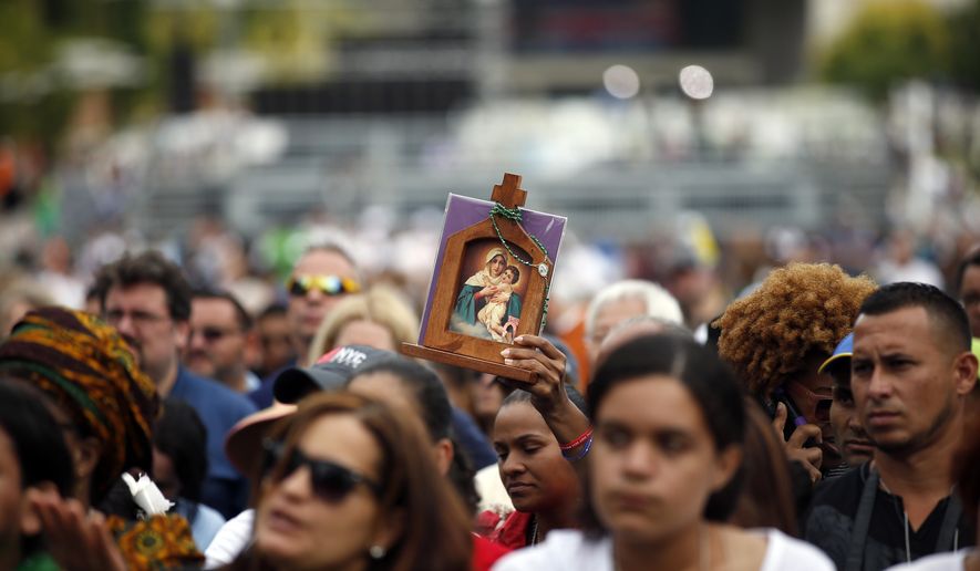 A woman holds an icon as she watches Pope Francis celebrate Mass on a large video monitor as people await the arrival of the pope at Independence Hall, Saturday, Sept. 26, 2015 in Philadelphia. (AP Photo/Alex Brandon)