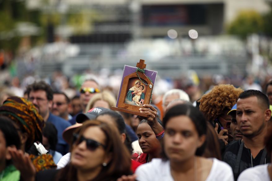 A woman holds an icon as she watches Pope Francis celebrate Mass on a large video monitor as people await the arrival of the pope at Independence Hall, Saturday, Sept. 26, 2015 in Philadelphia. (AP Photo/Alex Brandon)