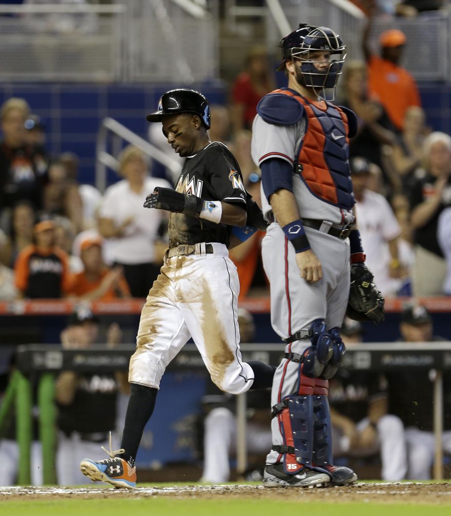 Miami Marlins' Dee Gordon, left, scores on a base hit by Martin Prado as Atlanta Braves catcher A.J. Pierzynski, right, looks on in the fifth inning of a baseball game, Sunday, Sept. 27, 2015, in Miami. Marlins' Miguel Rojas also scored on the hit. (AP Photo/Alan Diaz)